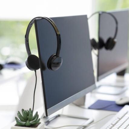 Headsets hang on powered-off computers in an empty office